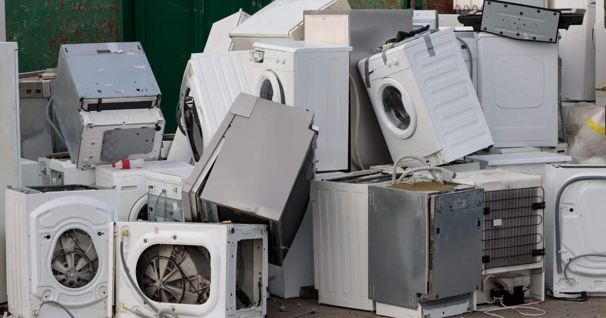 Haufen ausgedienter Haushaltsgeräte wie Waschmaschinen, Trockner und Geschirrspüler auf einem Recycling- oder Entsorgungsplatz.