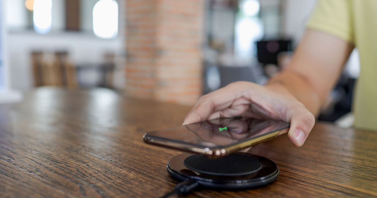 Hand legt ein Smartphone auf ein kabelloses Ladepad auf einem Holztisch.