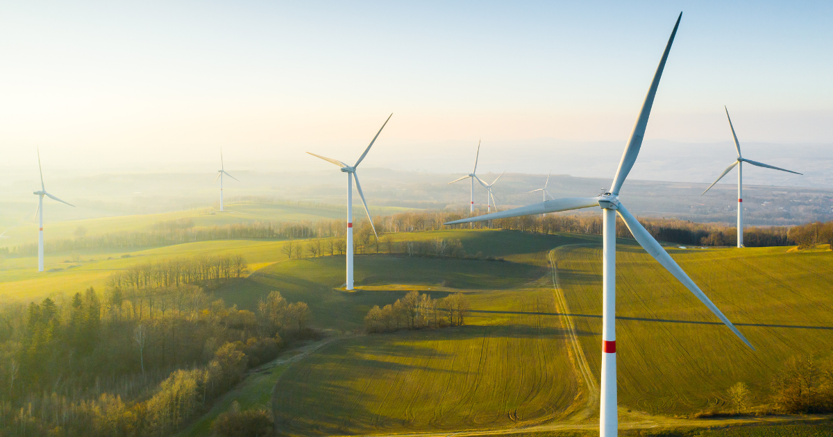 Windpark mit mehreren Windkraftanlagen auf sanften Hügeln in einer weitläufigen Landschaft bei goldenem Sonnenlicht.