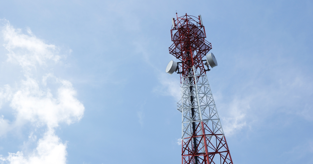 Hoher rot-weißer Funkturm mit mehreren Antennen vor blauem Himmel mit einigen Wolken.