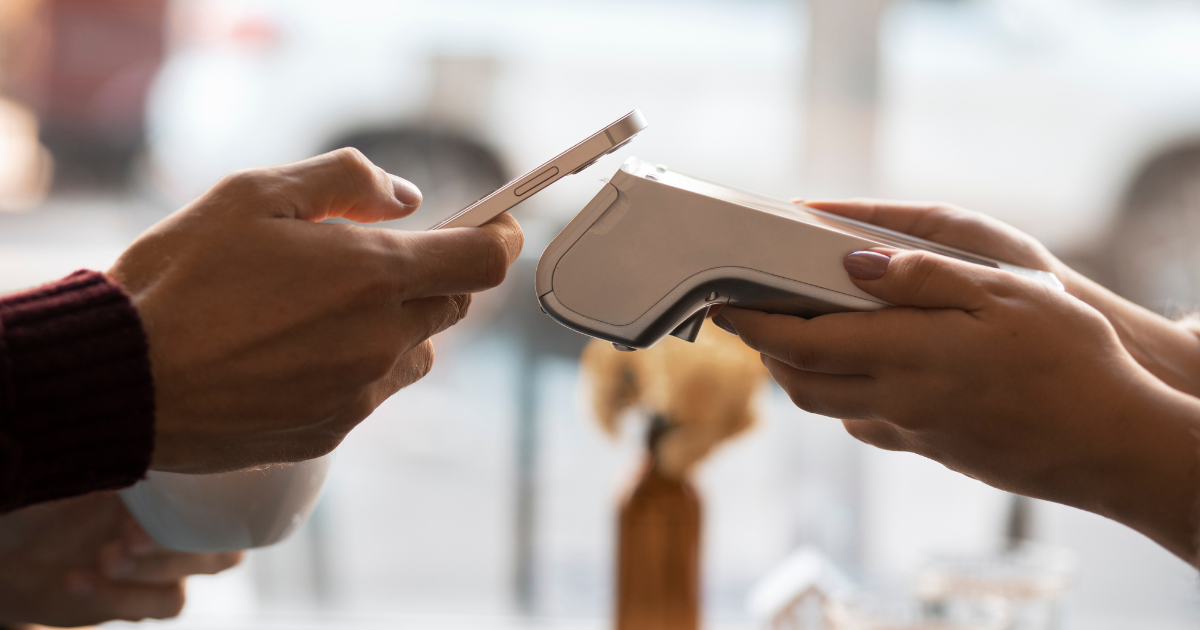 Eine Person hält ein Smartphone an ein mobiles Kartenlesegerät, das von einer anderen Person gehalten wird, um eine kontaktlose Zahlung durchzuführen.