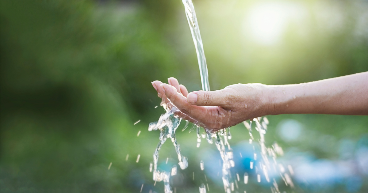 Nahaufnahme einer ausgestreckten Hand, über die klares Wasser fließt.