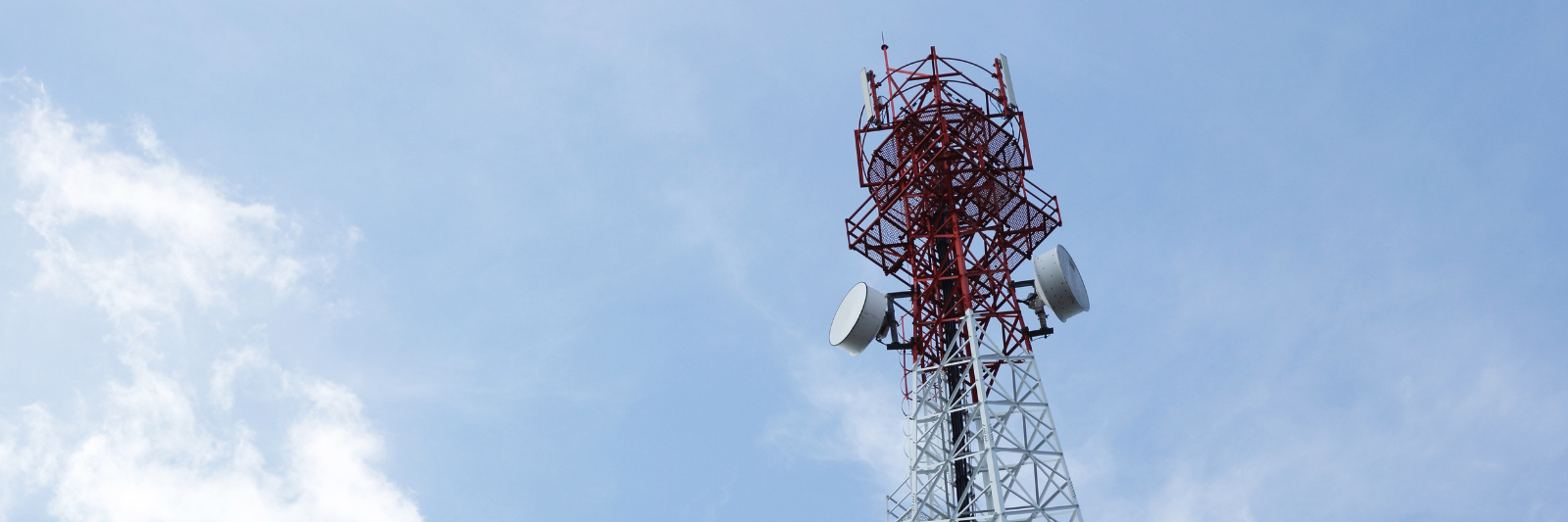 Hoher rot-weißer Funkturm mit mehreren Antennen vor blauem Himmel mit einigen Wolken.