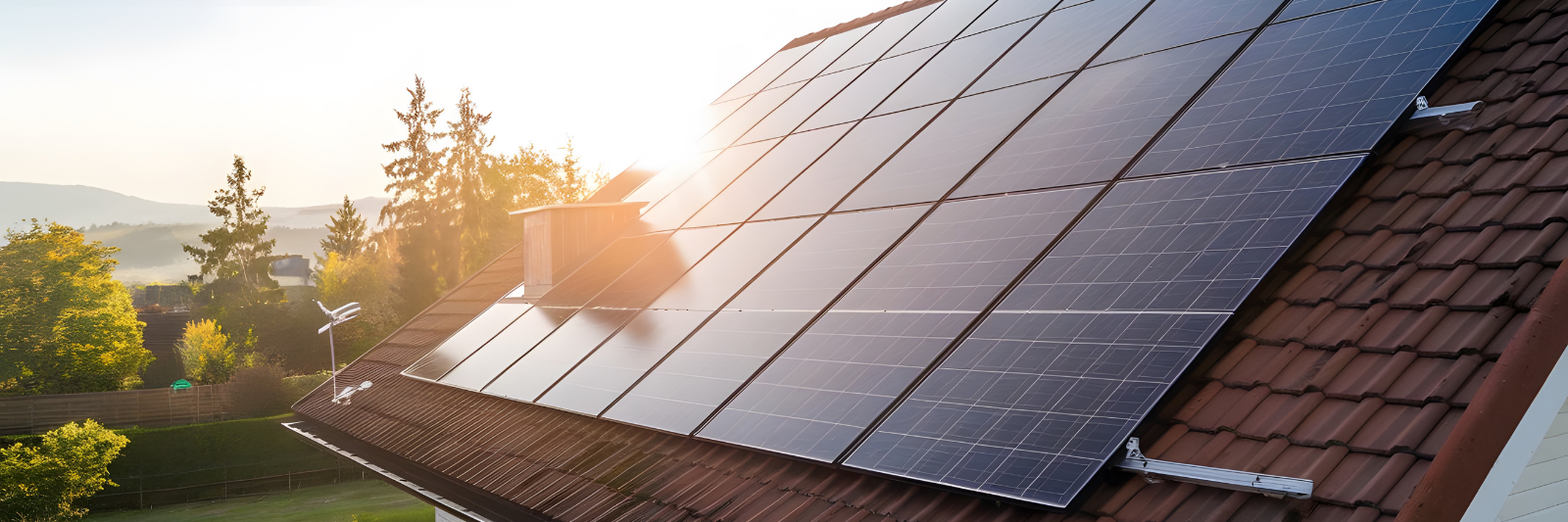 Solaranlage auf dem Dach eines Hauses bei Sonnenaufgang, umgeben von grüner Landschaft und Bäumen.
