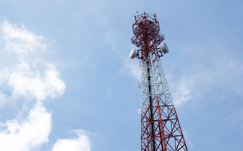 Hoher rot-weißer Funkturm mit mehreren Antennen vor blauem Himmel mit einigen Wolken.