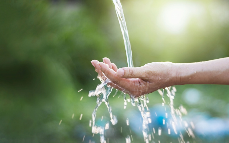 Nahaufnahme einer ausgestreckten Hand, über die klares Wasser fließt.