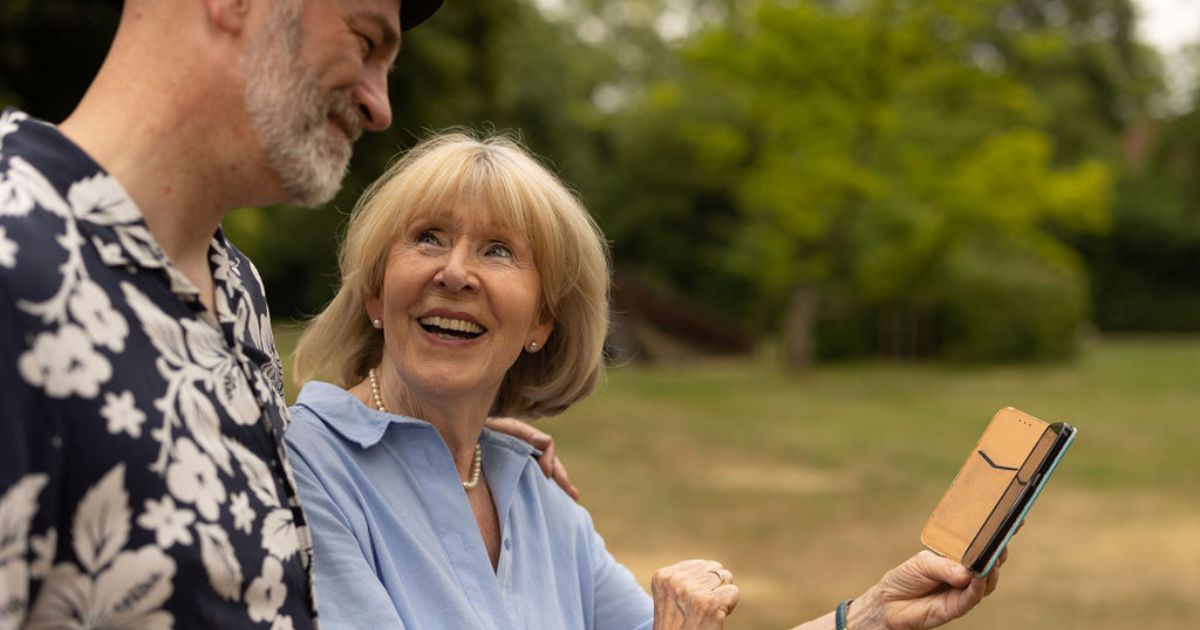 Frau und Mann sind am Handy, im Hintergrund Bäume im Park