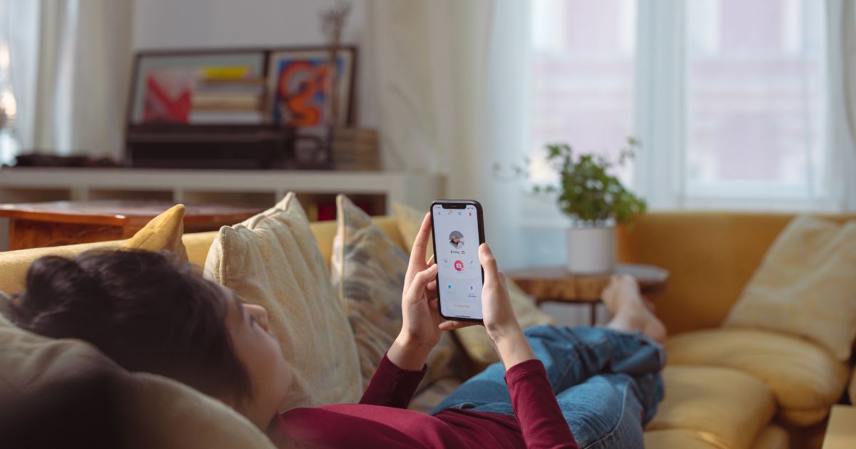 Frau liegt mit ihrem Handy auf dem Sofa, im Hintergrund ihre Wohnung