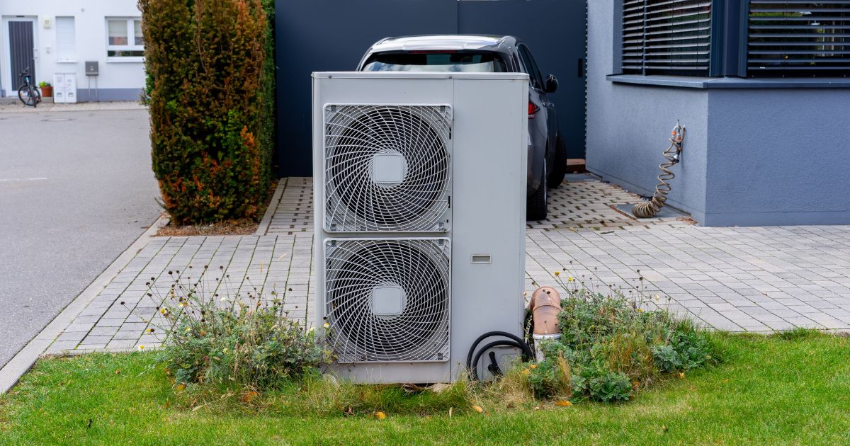Wärmepumpe vor Haus auf Wiese, dahinter Auto
