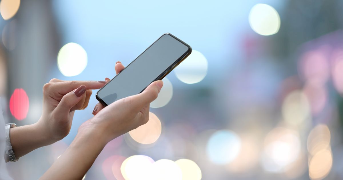 Handy wird in Hand gehalten, dahinter verschwommene Lichter
