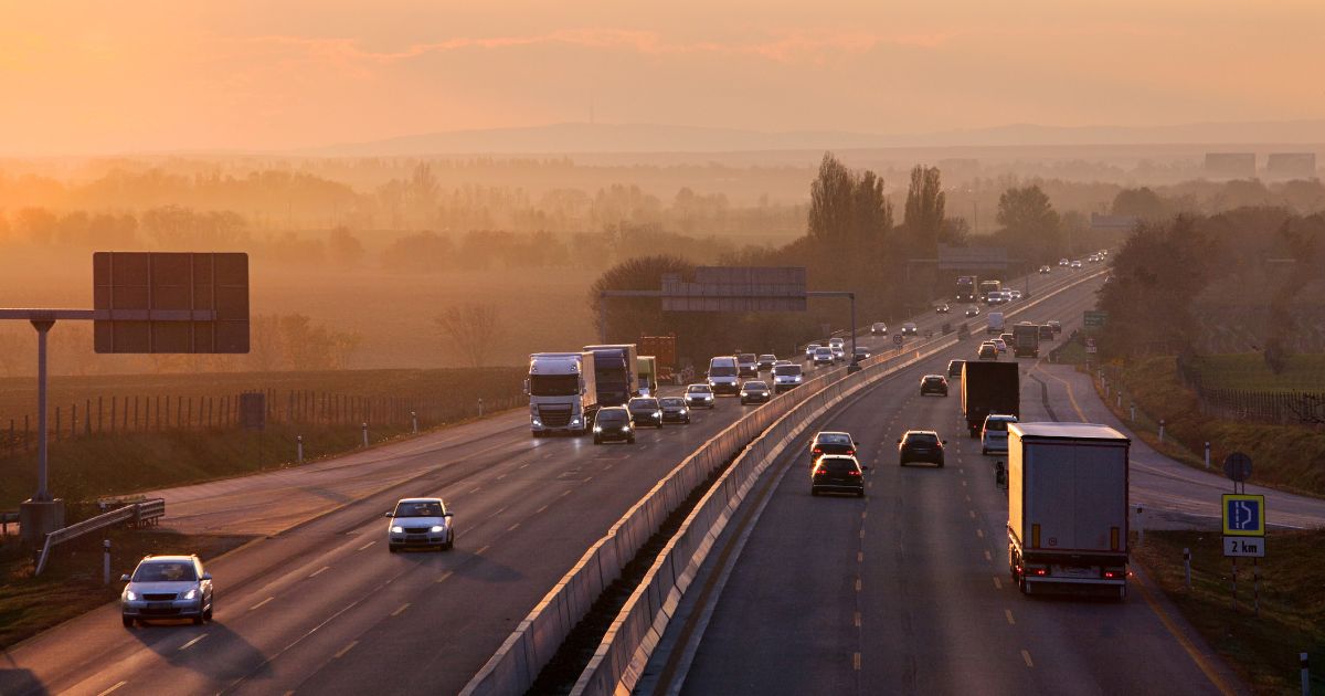 Autos und LKWs fahren auf einer Autobahn, daneben Bäume